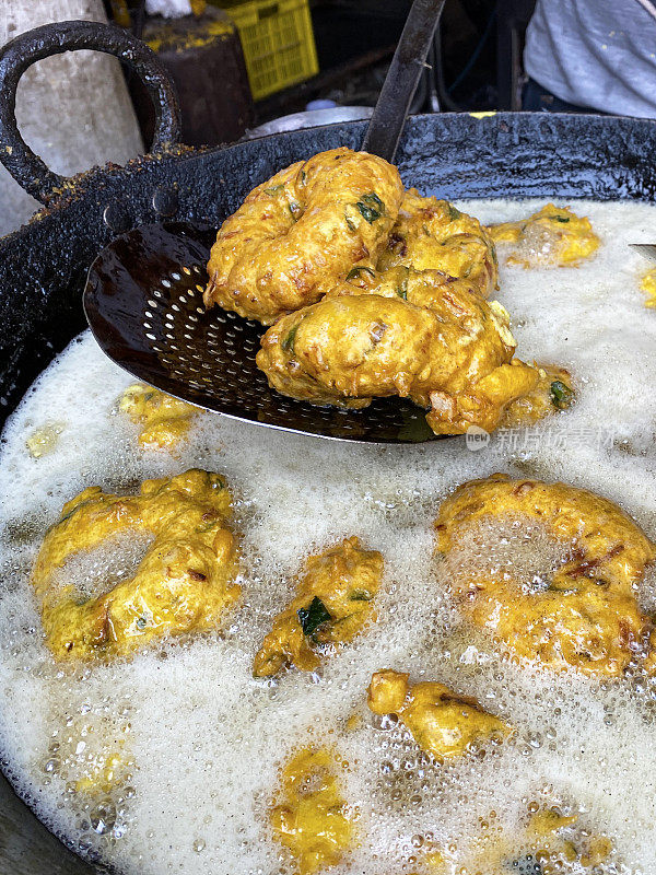 特写图片金色的Medu vada(软油条)早餐零食，街头小吃是在室外的炉子上做的，厨师用开槽的勺子转动由Vigna mungo(黑色扁豆)制成的美味甜甜圈，在煎锅里沸腾的油，上升，重点在前景